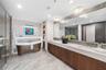 An en-suite bathroom featuring elegant finishes, dual vanities, a soaking tub and an oversized glass-enclosed shower.