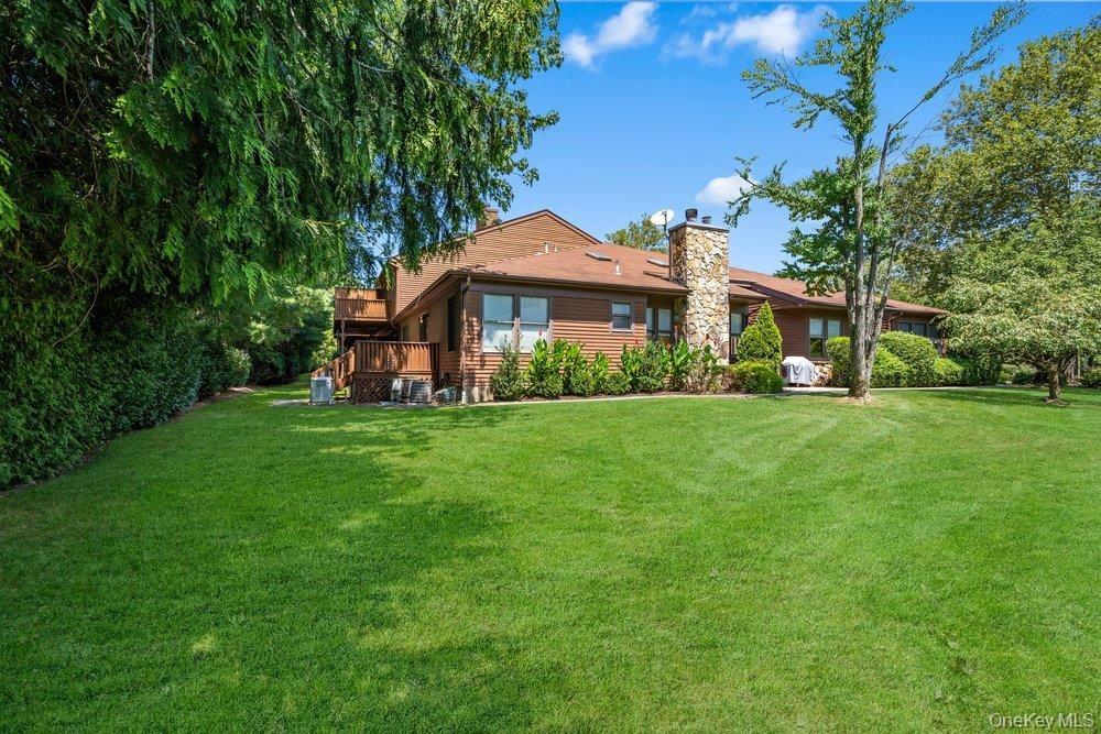 Expansive green lawn, mature trees, wood-sided exterior, stone chimney, and a multi-level wood deck
