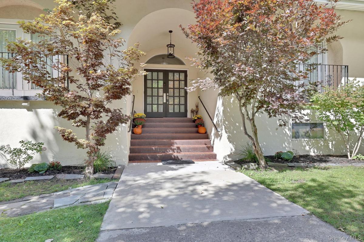 Arched entry with double-pane glass doors, complemented by a concrete walkway and mature landscaping
