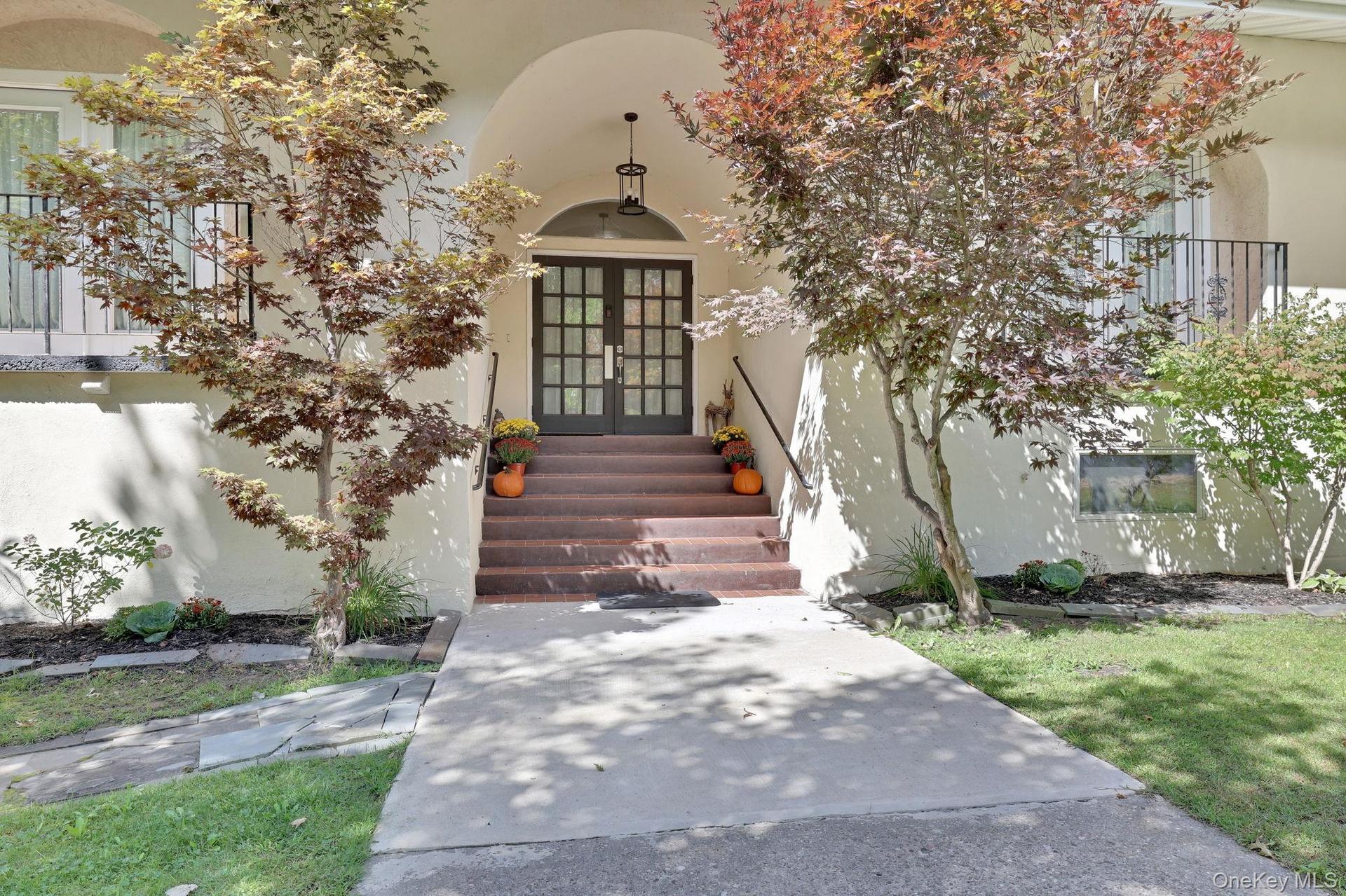 Arched entry with double-pane glass doors, complemented by a concrete walkway and mature landscaping