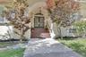 Arched entry with double-pane glass doors, complemented by a concrete walkway and mature landscaping