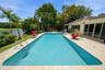A private outdoor retreat featuring a sparkling swimming pool, lush tropical landscaping, and serene water views.