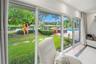 Floor-to-ceiling glass doors showcasing lush garden, pool, and tranquil water views.