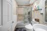 A beautifully appointed bathroom serving Secondary Bedrooms 2 and 3, featuring marble-inspired finishes, a glass-enclosed tub and shower, and a clean 