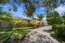 Front exterior featuring a spacious paved driveway, lush tropical landscaping, mature trees, and a private, inviting entrance.