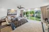 Expansive primary bedroom with floor-to-ceiling windows overlooking the lush garden and lake.