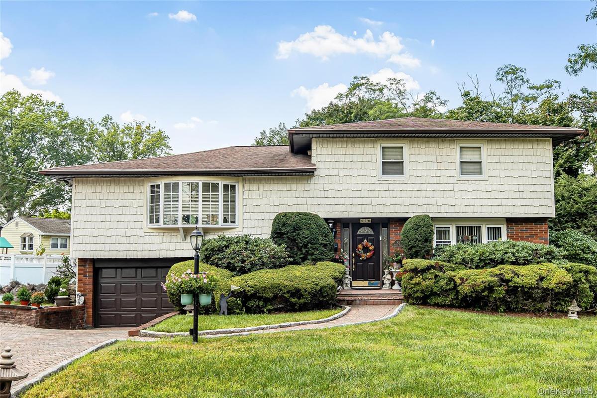 Split-level residence featuring brick and shake siding, an attached garage, a bay window, and a paver driveway