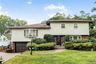 Split-level residence featuring brick and shake siding, an attached garage, a bay window, and a paver driveway