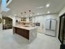 Kitchen featuring a large central island with a waterfall countertop, white cabinetry, a farmhouse-style apron sink, integrated lighting, and three pe