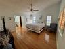 Wood-finish flooring, ceiling fan with integrated lighting, multi-pane window with wood-slat blinds, and louvered closet doors