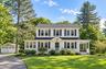 Two-story Colonial-style residence with white siding and dark shutters, featuring a covered front entry and a side porch