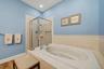 Built-in soaking tub, tiled surround, glass-enclosed shower, wall-mounted towel bar, and recessed lighting