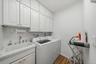 White cabinetry with gold-tone hardware, utility sink with chrome  faucet, white square tile backsplash, wood-finish flooring
