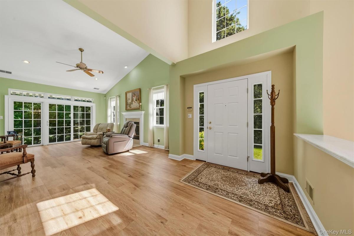 Vaulted ceiling with recessed lighting, wood-finish flooring, white  fireplace, multiple large windows, and a front entry door with sidelights