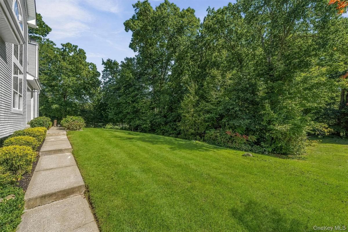 Expansive lawn with mature trees and established landscaping,  bordered by a concrete walkway and a shingled exterior