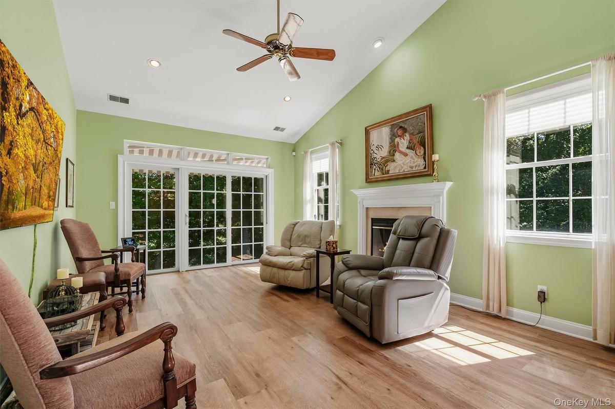 Vaulted ceiling with a ceiling fan and recessed lighting, wood-finish  flooring, a white fireplace mantel, and sliding glass doors