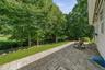 Paver patio with a stone retaining wall, adjacent to a sloped lawn and mature trees