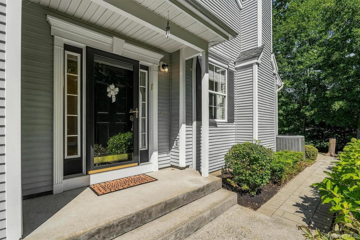 Paneled front door with sidelight windows, covered entry, concrete  steps, horizontal siding, and a paver walkway