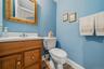 Wood-finish flooring, light wood vanity with brass hardware, white countertop with integrated sink, chrome faucet, and a toilet