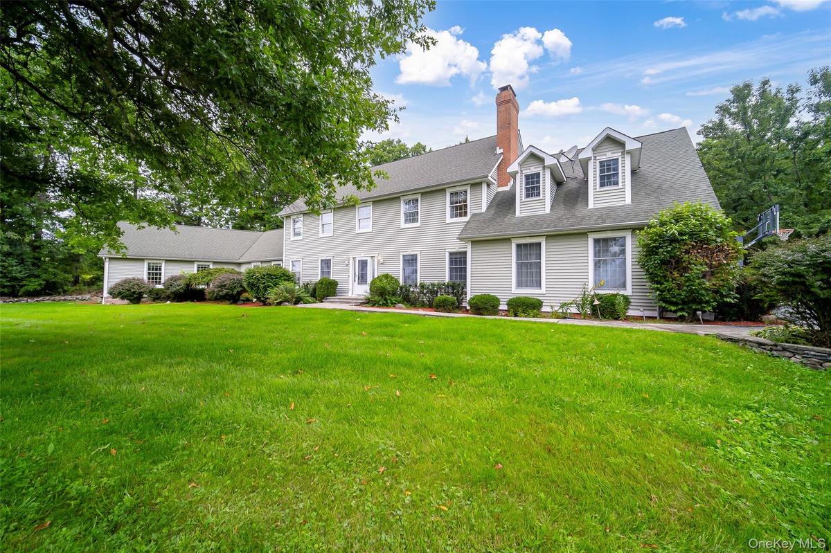 Expansive front yard with a stone retaining wall, mature trees, and well manicured landscaping including established shrubs