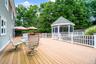 Expansive outdoor deck featuring a screened gazebo, white railing system, and adjacent green space