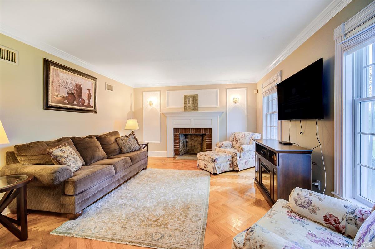 Living room area featuring herringbone wood flooring, crown molding, a brick fireplace with a white mantel, and large windows with white trim