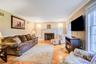 Living room area featuring herringbone wood flooring, crown molding, a brick fireplace with a white mantel, and large windows with white trim