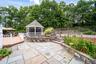 Stone patio with a screened gazebo, adjacent wood deck, and stone water feature