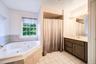 Corner soaking tub with tiled surround, single vanity, and tiled flooring