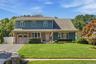 Curb view of home with one car garage, oversized driveway, brick and shingle with covered porch.