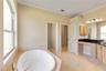 View of soaking tub, toilet room (left pocket door), linen closet, and right opening (also a pocket door) leads to the primary bedroom.