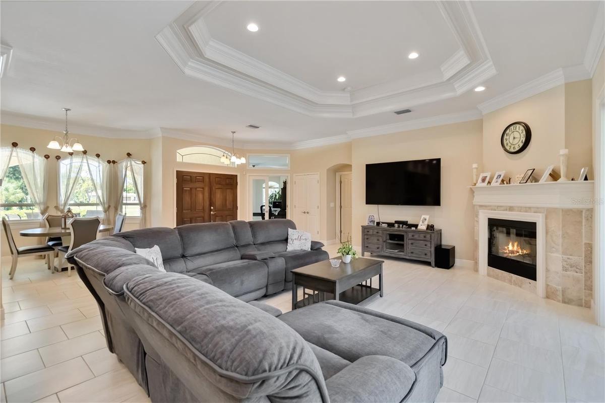 Another view of the open floor plan, tray ceiling, and wood fireplace. The open door th the right of the closet leads to the primary bedroom. This hom