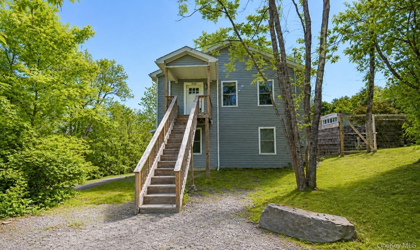 Front entry with covered stoop, exterior staircase, gravel driveway and mature shade trees.