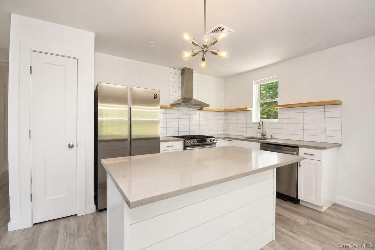 Kitchen with white shaker cabinetry, center island with seating overhang, stainless steel appliances, wall-mounted range hood, subway tile backsplash 