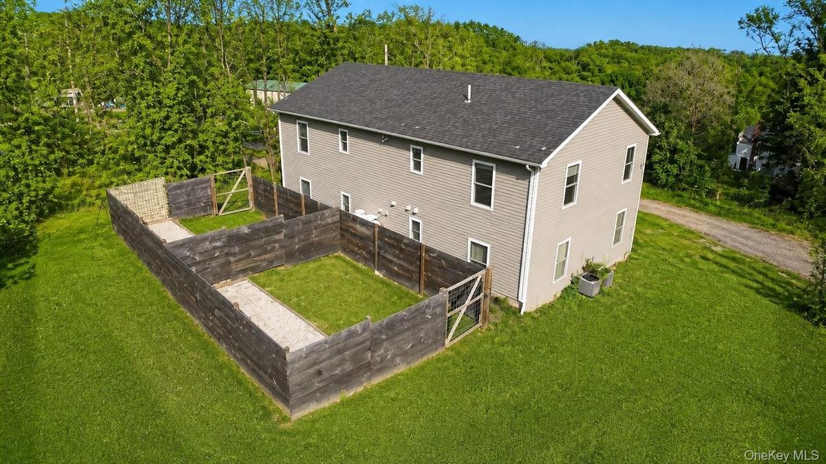 Elevated view of the home and fully fenced backyard area, bordered by lawn and mature trees.