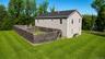 Aerial view from the side showing the level lawn, wood privacy-fenced yard area and wooded surroundings.
