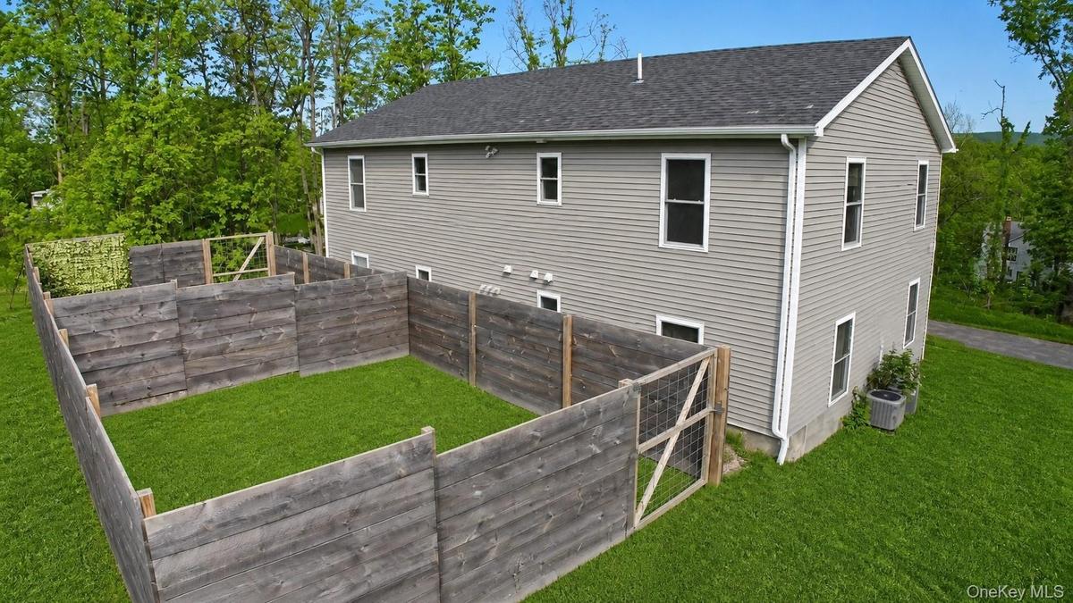 Aerial view of the rear of the home showing the two-story layout, wood-fenced backyard enclosure and open lawn.