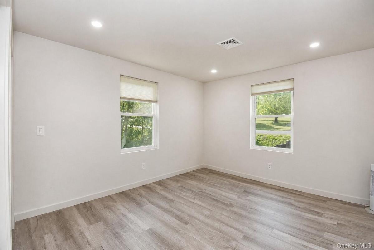 Bedroom with two windows, recessed lighting and wood-look plank flooring.