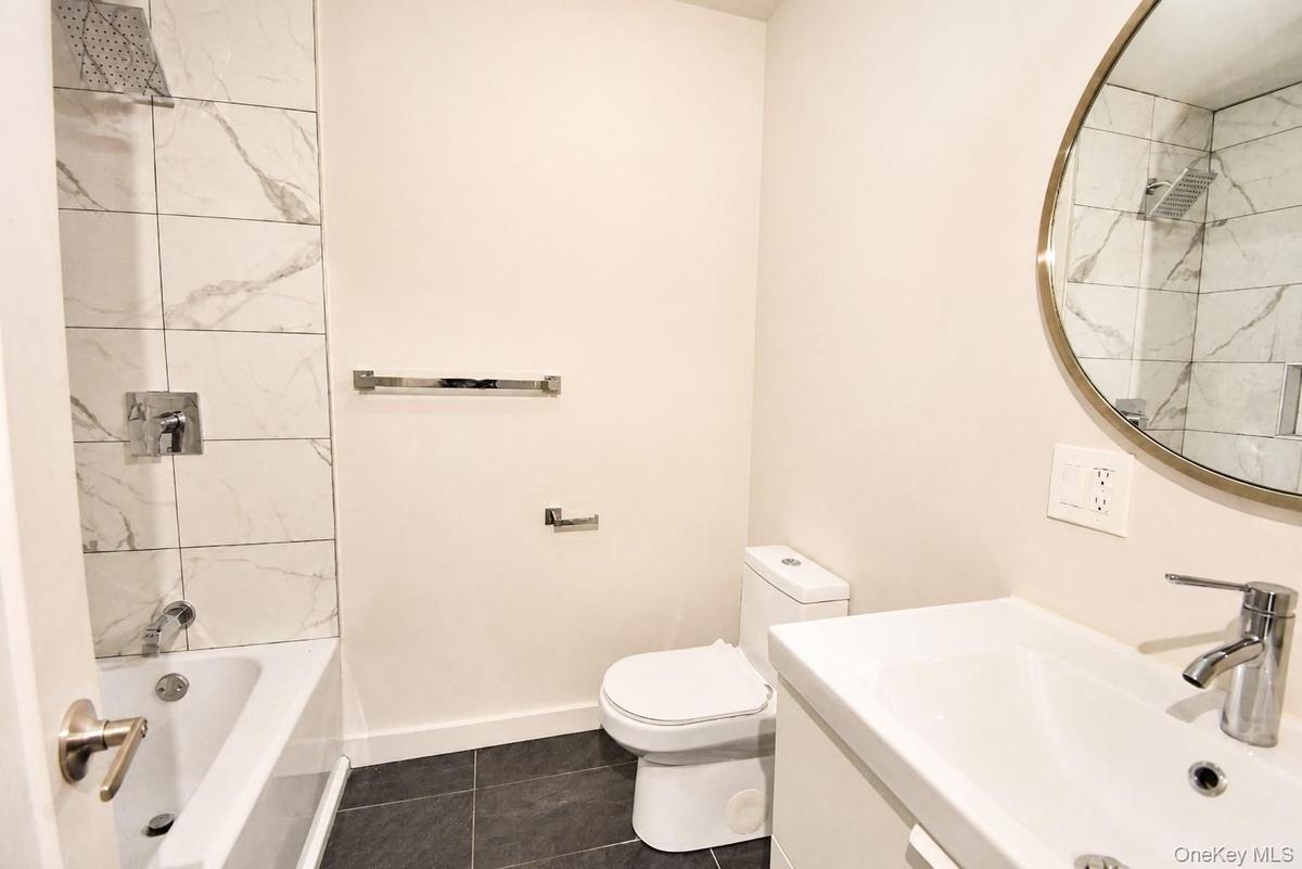 Full bathroom with tub/shower, tiled surround, floating vanity, round mirror and tile floor.