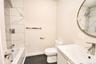 Full bathroom with tub/shower, tiled surround, floating vanity, round mirror and tile floor.