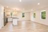 Living and dining area viewed from the kitchen, with windows on two walls and wood-look flooring.