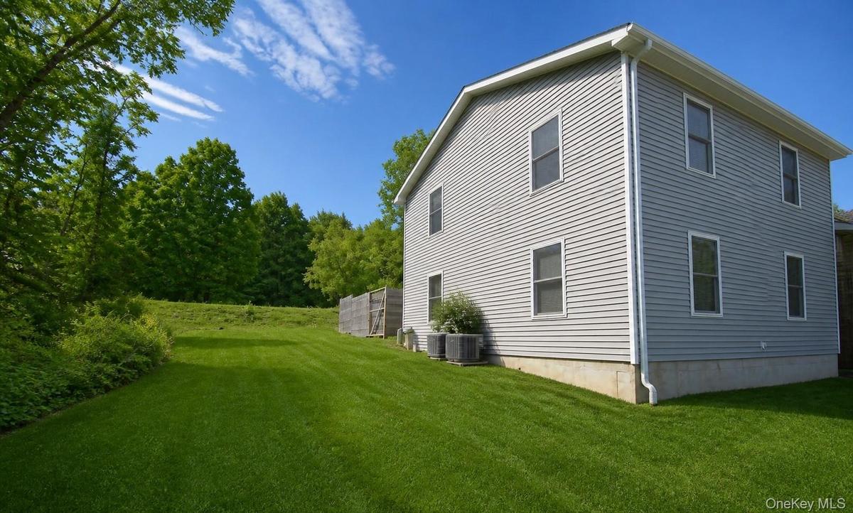 Side elevation with multiple windows, level lawn and wooded backdrop.