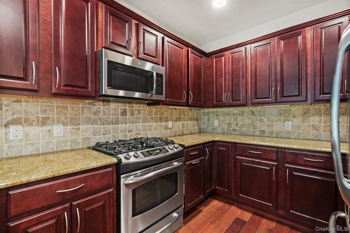 Cherry wood cabinetry, stainless steel range, stainless steel microwave, stone countertops, and a tile backsplash