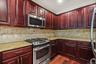 Cherry wood cabinetry, stainless steel range, stainless steel microwave, stone countertops, and a tile backsplash