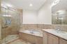 Glass-enclosed shower with a handheld shower fixture, built-in bathtub, single vanity with light wood cabinetry, and a full-width mirror