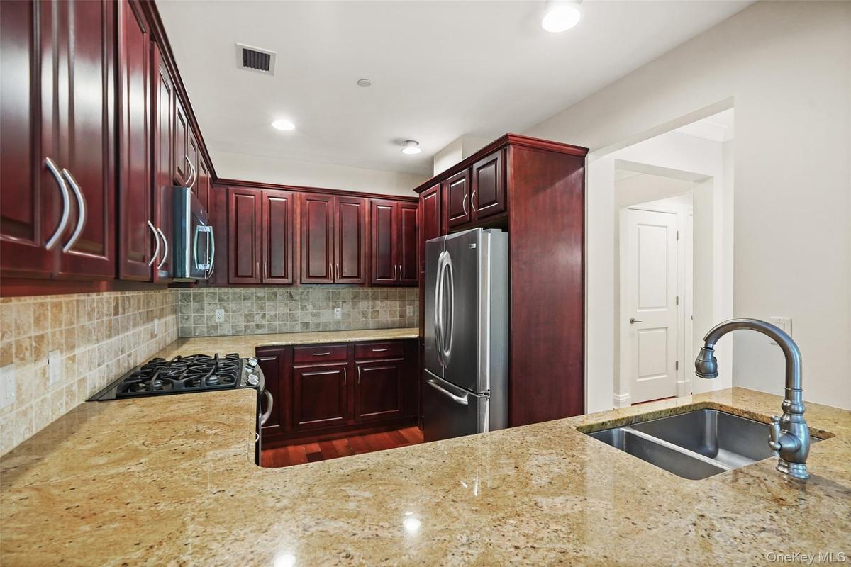 Rich wood-finish cabinetry with curved pulls, stainless steel appliances, speckled stone countertops, and a tile backsplash