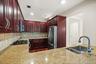 Rich wood-finish cabinetry with curved pulls, stainless steel appliances, speckled stone countertops, and a tile backsplash