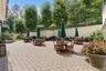 Expansive paver patio with a low retaining wall, black wrought iron fencing, mature trees, and landscaping