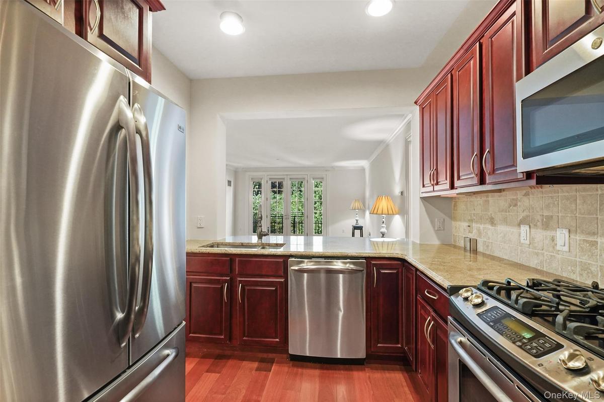 Kitchen featuring stainless steel appliances, wood-finish flooring, cherry-stained cabinetry, light-toned countertop, and tiled backsplash