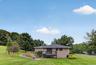 Expansive green lawn, multi-level composite deck, stone retaining wall, mature trees, and a paved street